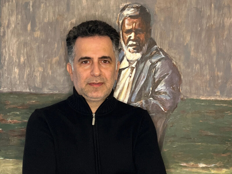 Das Foto zeigt Reza Ghanei vor einem seiner gemalten Bilder