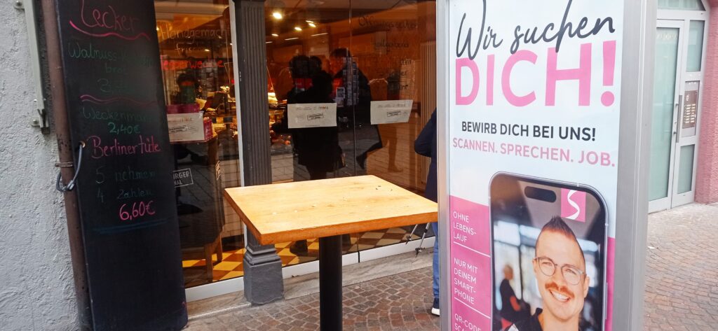 Das Foto zeigt eine Bäckerei in der Innenstadt und ein Plakat mit der Aufschrift: Wir suchen dich!