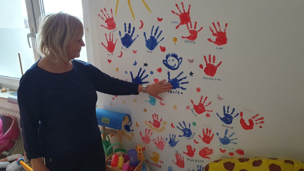 Die Konstanzer Tagesmutter Mario Romano vor einer Wand mit bunten Handabdrücken von Kindern.