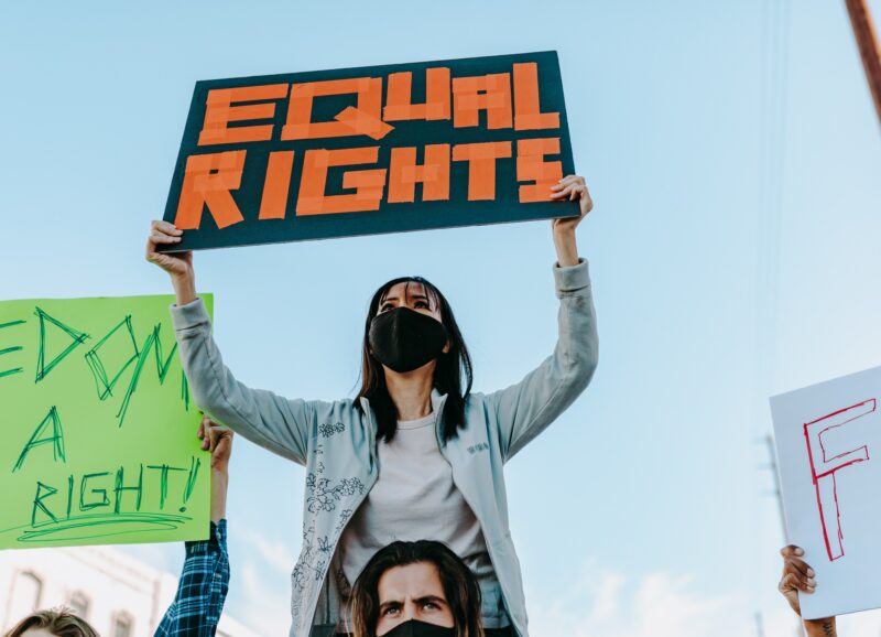 Das Bild zeigt eine Frau bei einer Demonstration mit einem Schild auf dem Equal Rights steht.