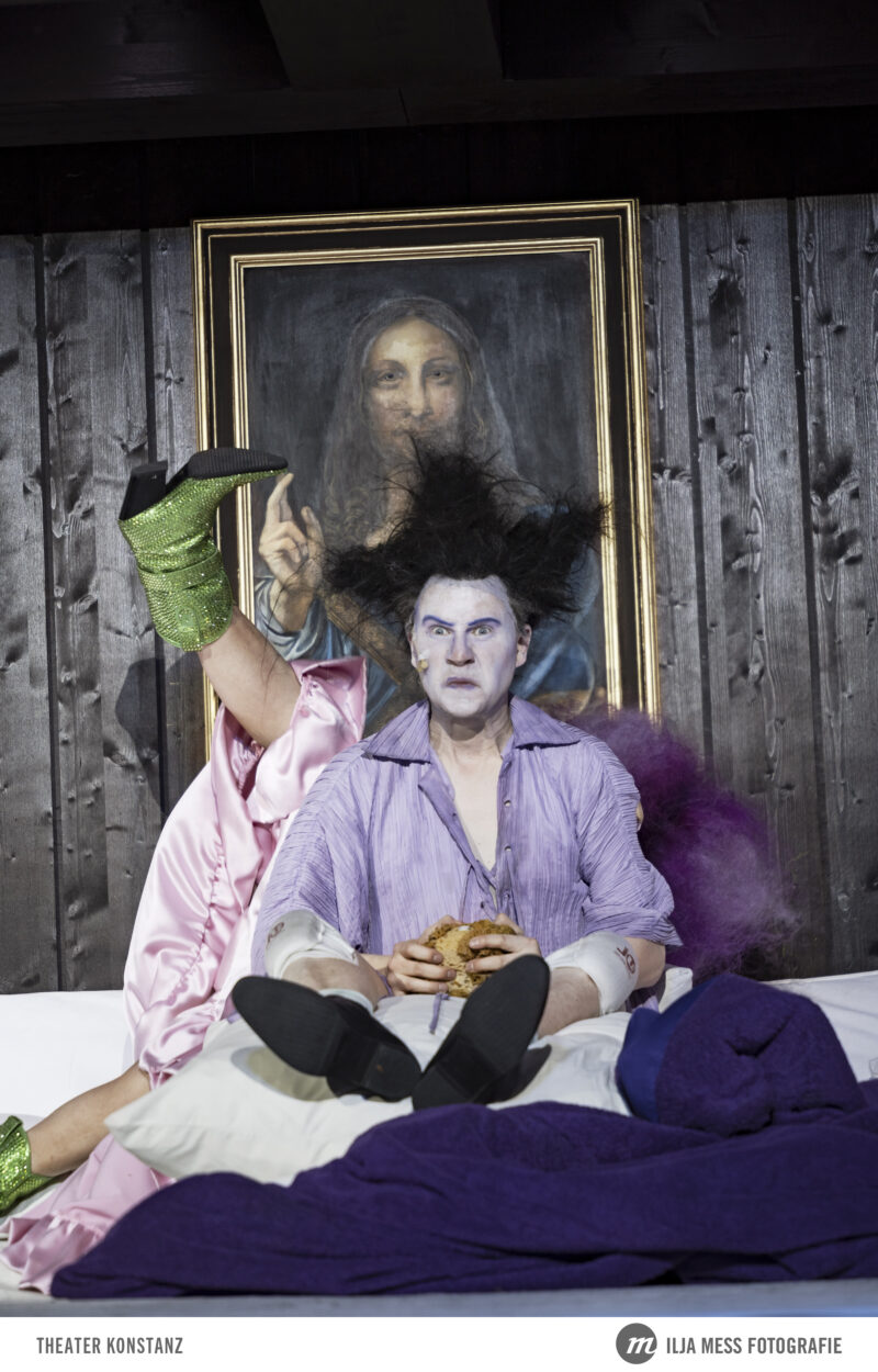 Das Bild zeigt eine Szene aus dem Theaterstück "Der eingebildete Kranke" am Theater Konstanz. Zu sehen ist die Hauptfigur Argan auf dem Bett mit grimmigem Blick.