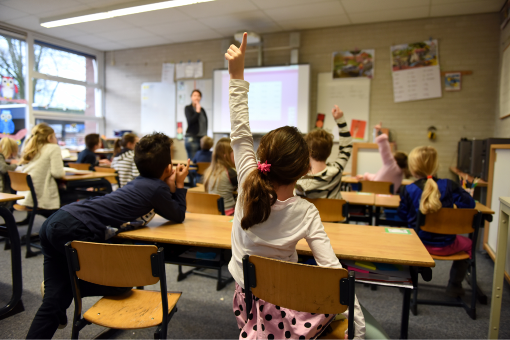 Schulsituation in einem Klassenzimmer. Eine Schülerin zeigt auf.
