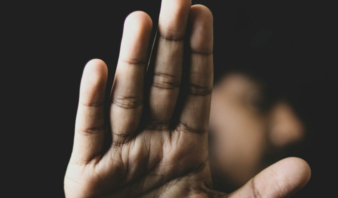 Eine ausgestreckte Hand in Stopp-Geste, unscharfer Hintergrund mit angedeuteter Person – Symbolbild für Grenzsetzung und Schutz vor Übergriffen.