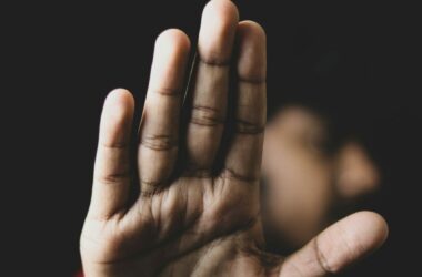 Eine ausgestreckte Hand in Stopp-Geste, unscharfer Hintergrund mit angedeuteter Person – Symbolbild für Grenzsetzung und Schutz vor Übergriffen.