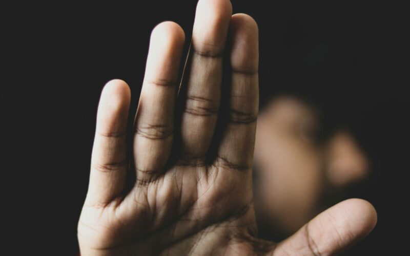 Eine ausgestreckte Hand in Stopp-Geste, unscharfer Hintergrund mit angedeuteter Person – Symbolbild für Grenzsetzung und Schutz vor Übergriffen.