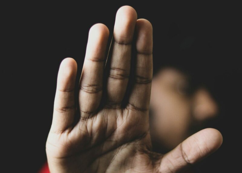 Eine ausgestreckte Hand in Stopp-Geste, unscharfer Hintergrund mit angedeuteter Person – Symbolbild für Grenzsetzung und Schutz vor Übergriffen.